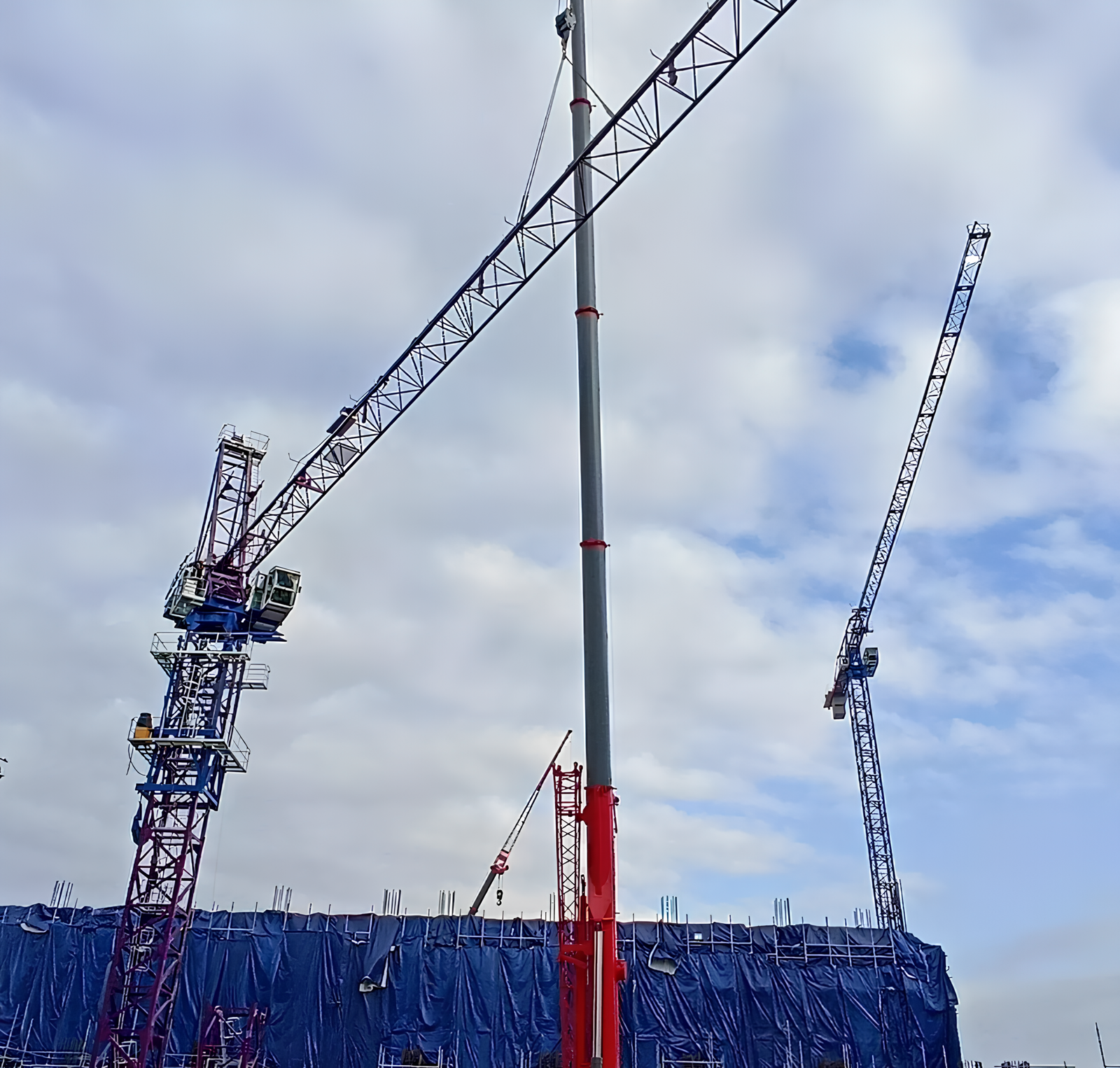 VEGA tower cranes lifting heavy materials at a construction site, cloudy sky background