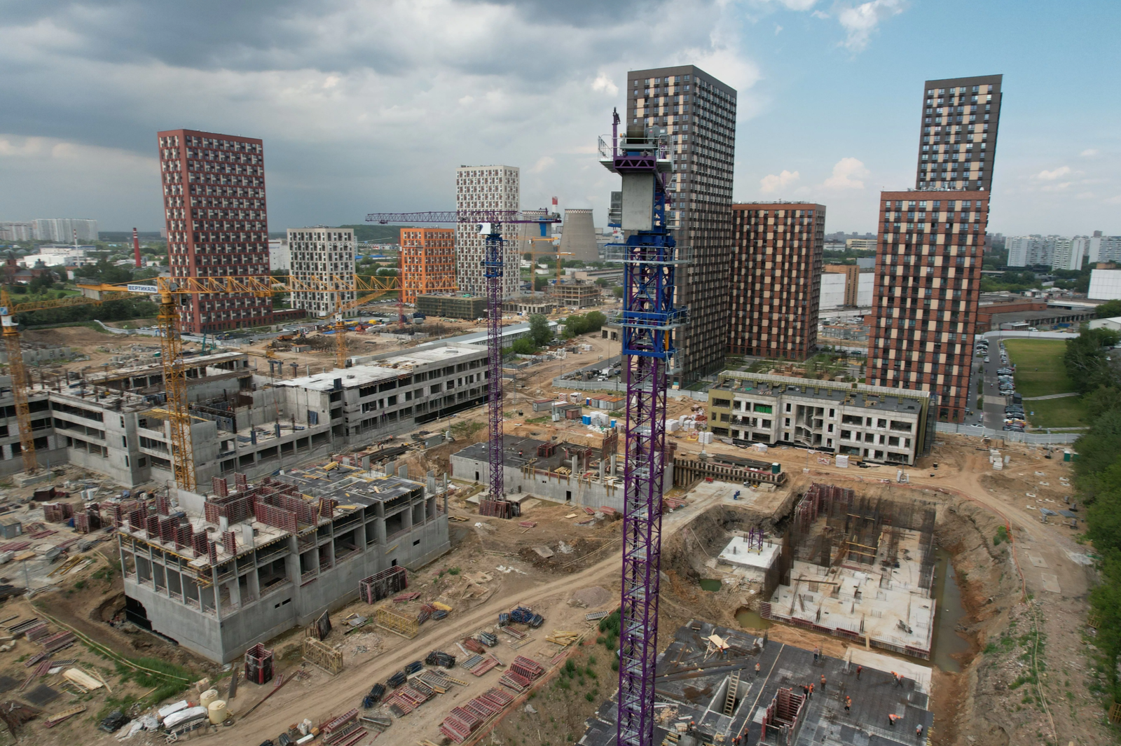 Construction site with multiple tower cranes, modern buildings in the background, and ongoing urban development.