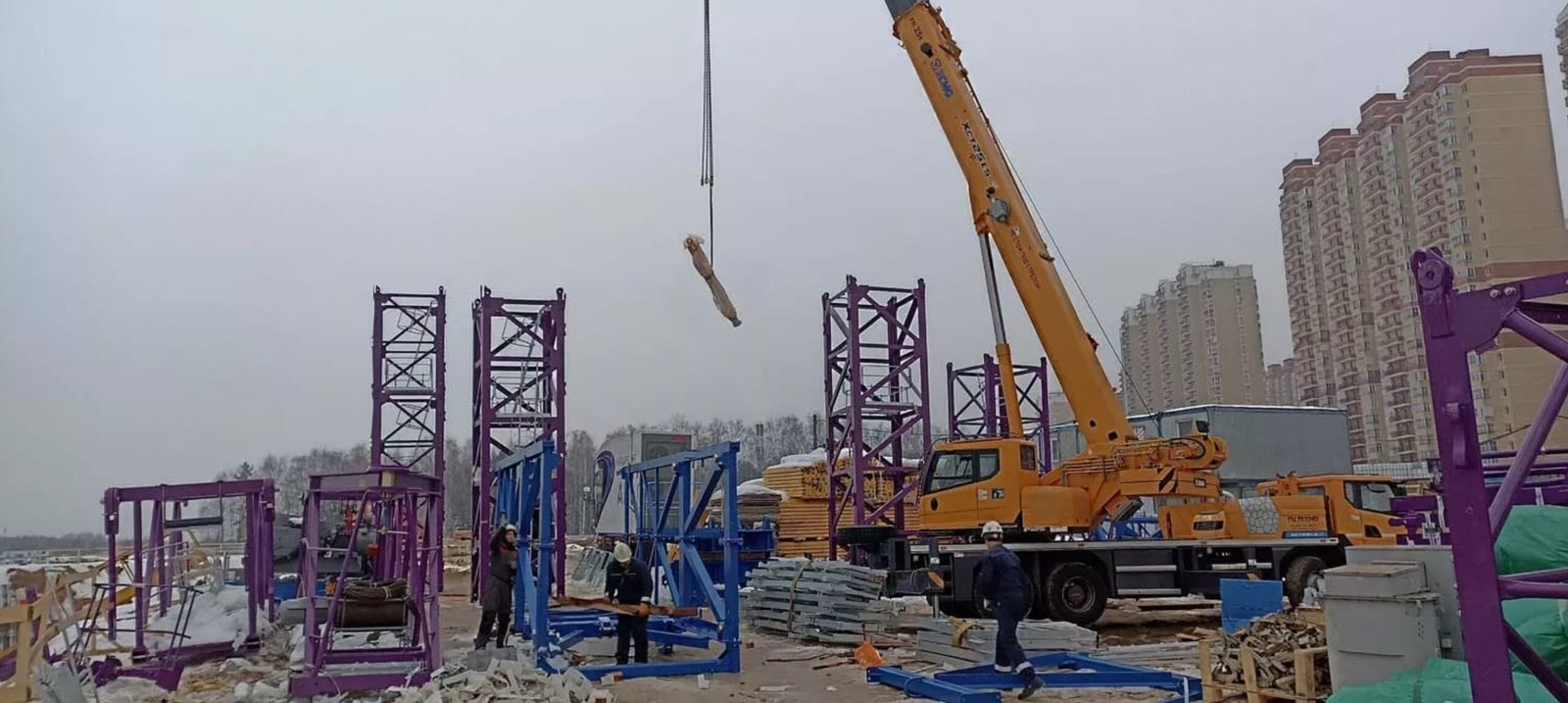 Assembly of tower crane components on-site, with workers and a mobile crane in action.